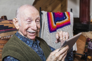 Smiling older gentleman working on a tablet in his living-room