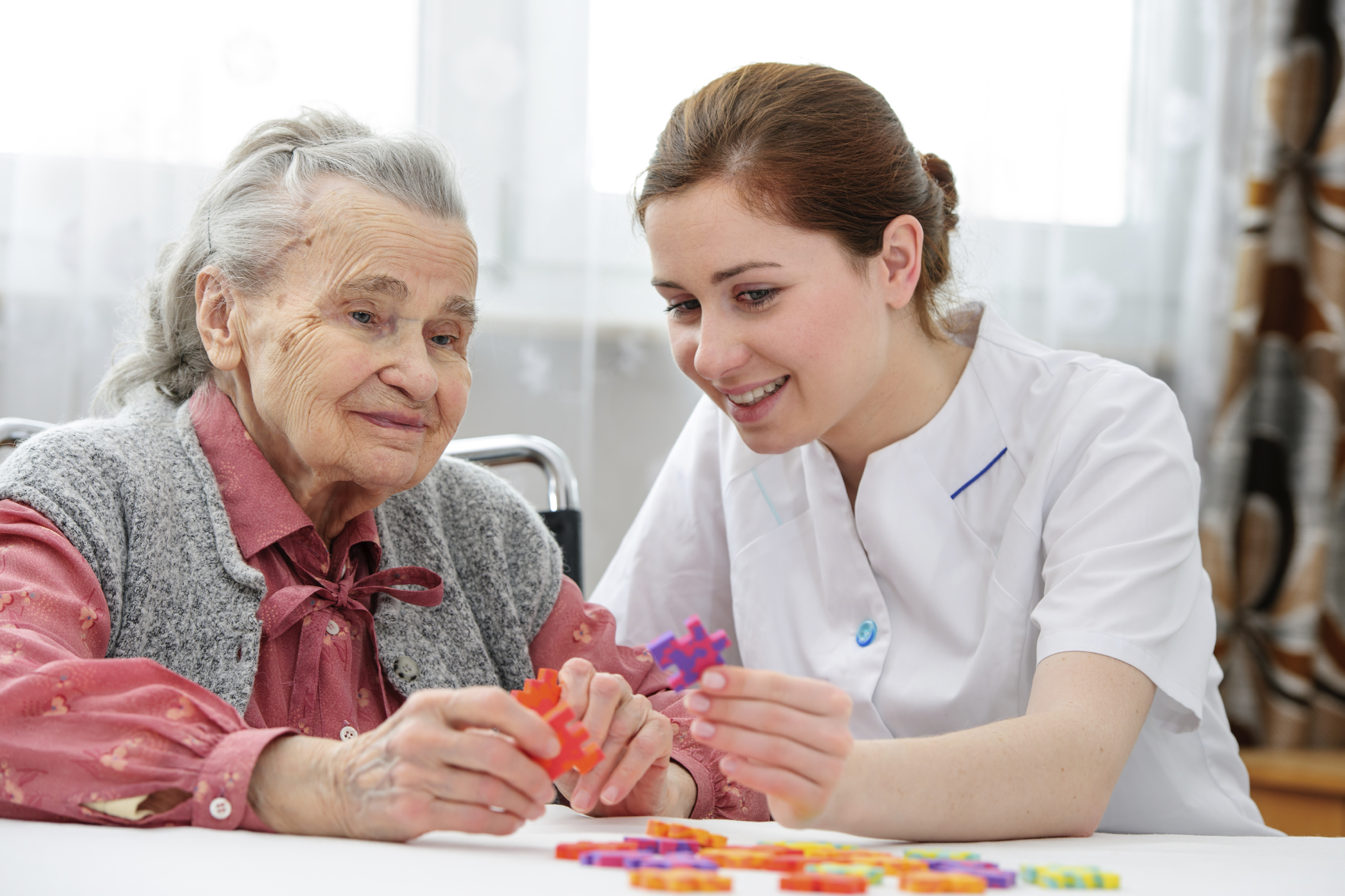 Elder care nurse playing jigsaw puzzle with senior woman in nursing home