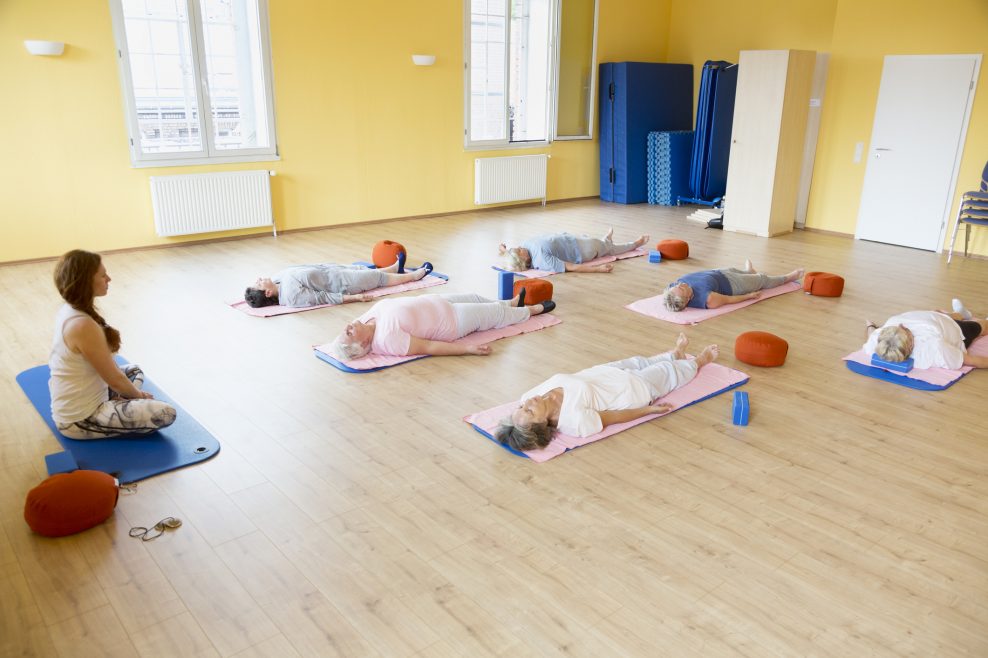 Yoga class with senior women lying down on exercise mat, relaxation exercise